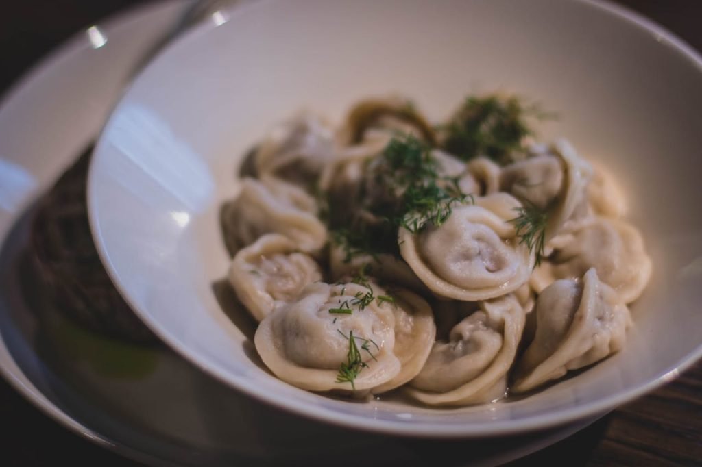 A close-up of delicious homemade dumplings garnished with fresh dill in a white bowl.
